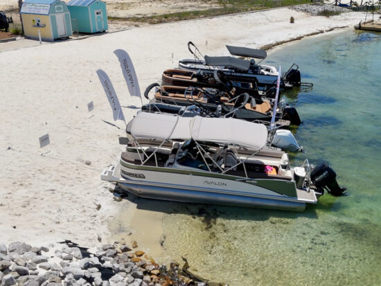 A row of pontoon boats moored at a sandy marina in Fort Walton Beach, with clear turquoise water and beach amenities visible in the background.