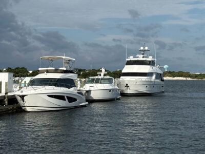 Luxury yachts docked at marina transient slips under partly cloudy skies in Fort Walton Beach, with calm waters and a scenic backdrop of lush greenery and distant water views.