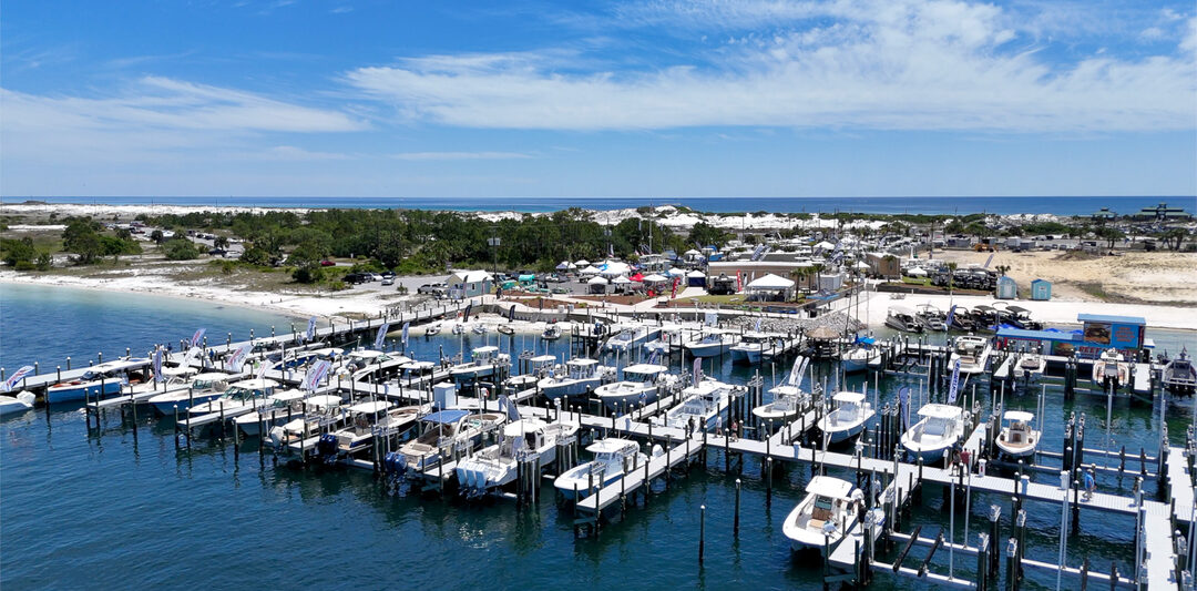 Aerial view of a marina in Fort Walton Beach, showcasing numerous boats docked at the piers, set against a backdrop of clear blue skies and lush greenery along the shoreline.