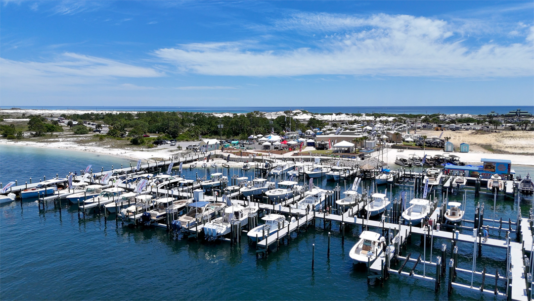 Aerial view of a marina in Fort Walton Beach, showcasing numerous boats docked at the piers, set against a backdrop of clear blue skies and lush greenery along the shoreline.