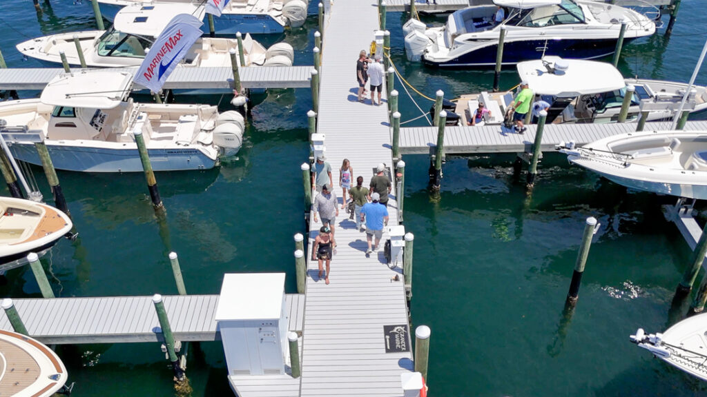 Aerial view of a bustling marina in Fort Walton Beach, showcasing boats docked at piers and visitors strolling along the walkways under clear skies.