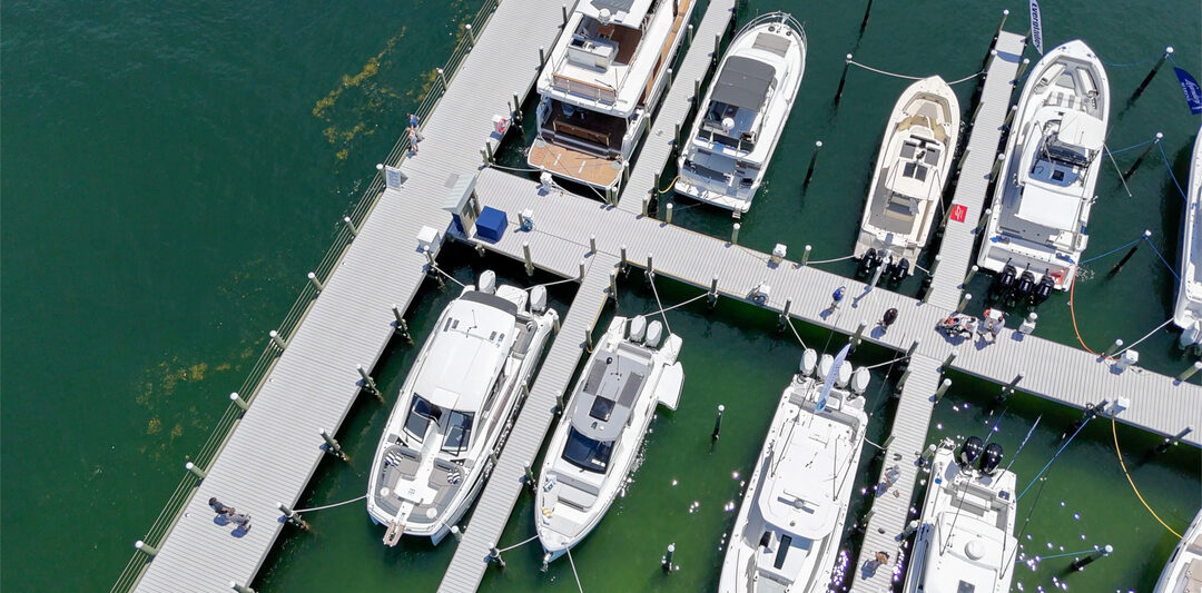 Aerial view of a marina in Fort Walton Beach with multiple luxury yachts and boats docked at a well-maintained pier in clear emerald waters.
