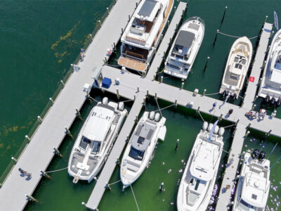 Aerial view of a marina in Fort Walton Beach with multiple luxury yachts and boats docked at a well-maintained pier in clear emerald waters.