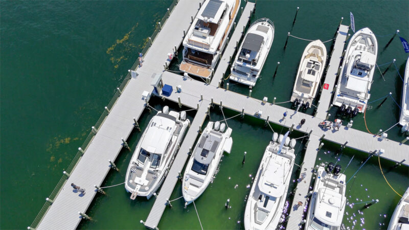 Aerial view of a marina in Fort Walton Beach with multiple luxury yachts and boats docked at a well-maintained pier in clear emerald waters.