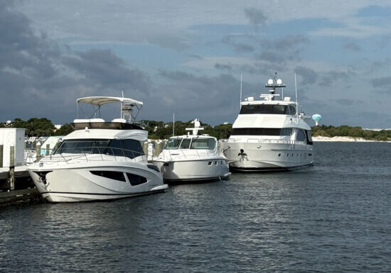 Luxury yachts docked at marina transient slips under partly cloudy skies in Fort Walton Beach, with calm waters and a scenic backdrop of lush greenery and distant water views.