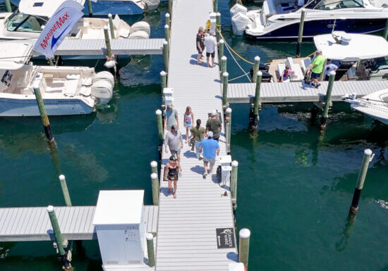 Aerial view of a bustling marina in Fort Walton Beach, showcasing boats docked at piers and visitors strolling along the walkways under clear skies.